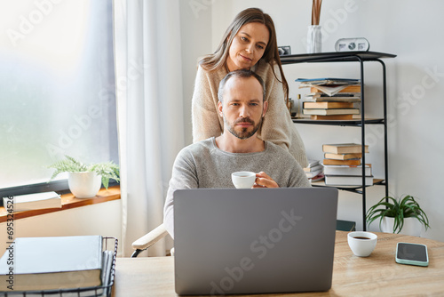 caring woman supporting thoughtful husband sitting with coffee cup at laptop in home office photo