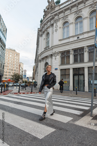 Beautiful young fashion model girl in fashion urban clothes walks in the city at a pedestrian crossing