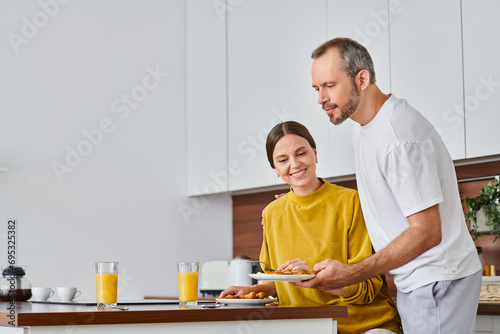 husband serving delicious breakfast near pleased wife in kitchen, morning of child-free couple