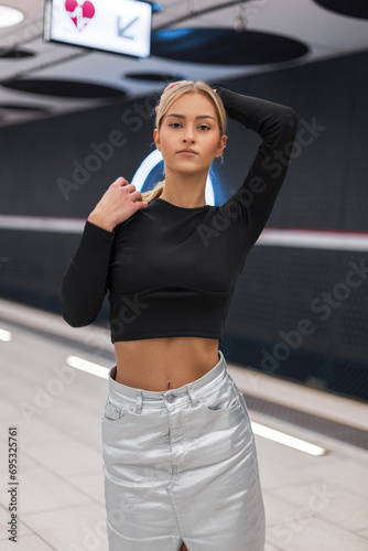 Fashion beautiful model girl in a black top stands and looks at the camera at a modern metro station