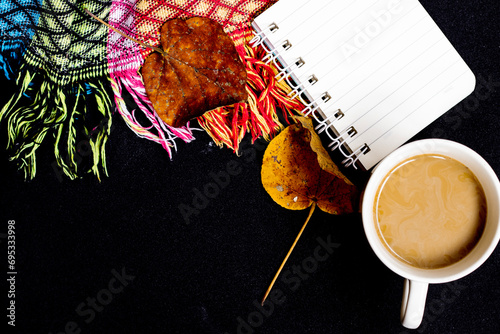The comfort of being at home in autumn. The photo above is of a cup of hot coffee, a patchwork blanket, maple leaves, on a black isolated background with copy space