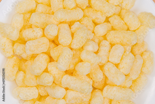 Heap of sweet corn puffs on white plate, top view