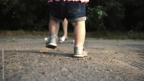 A small child takes his first steps. Mom and child walk in the fresh air. The concept of children's first steps and child growing up and development. Mom and little daughter, child's feet close-up  photo