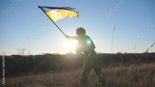 Dolly shot of male military in uniform waving flag of Ukraine at sunset. Young soldier of ukrainian army lifting national banner as symbol of victory against russian aggression. Invasion resistance photo