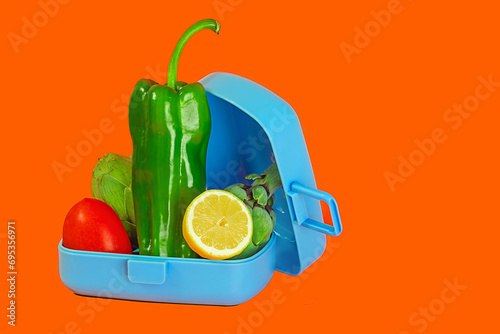 Fresh vegetables in a blue lunch box on an orange background photo
