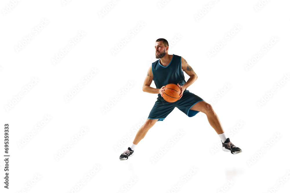 Full length portrait of athletic man, professional basketball player actively training before match against white background.