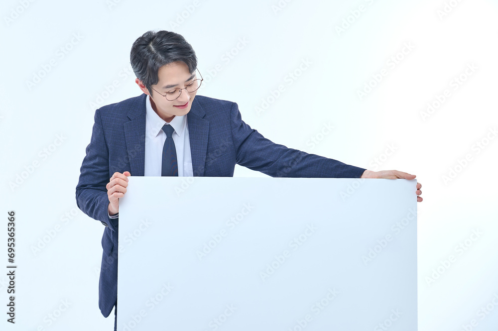 A handsome Asian man wearing a suit and glasses is holding a white sign and making various facial expressions and gestures. A handsome Asian man wearing a suit and glasses is holding a white sign and making various facial expressions and gestures.