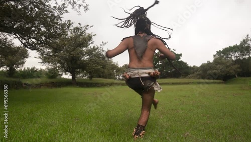 Man in body paint and traditional clothes with dreadlocks performing a traditional Mayan war dance, captured mid-movement in a lush green environment, embodying the ancient rituals of Mexico photo