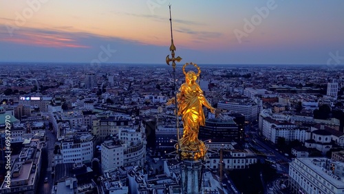 Aerial view of the statue of the Madonna on the central spire of the Duomo and the city's cathedral at dawn. Roofs of houses and skyscrapers. Sun over the horizon. duomo square. Italy Milan 16.11.2023 photo
