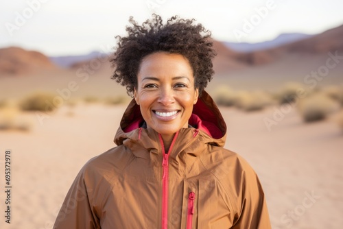 Portrait of a jovial afro-american woman in her 40s wearing a lightweight packable anorak against a backdrop of desert dunes. AI Generation