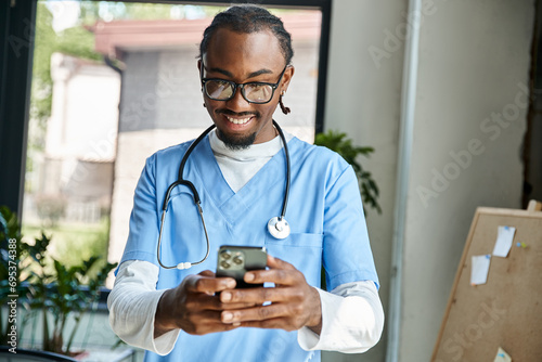 handsome happy african american doctor with stethoscope looking at his mobile phone, telemedicine