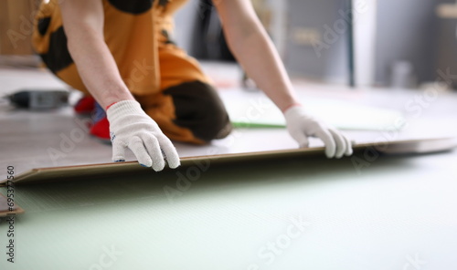 Fototapeta Naklejka Na Ścianę i Meble -  Close-up of adult man installing new laminated wooden floor in room. Professional worker in protective white gloves. Qualified foreman. Construction site concept