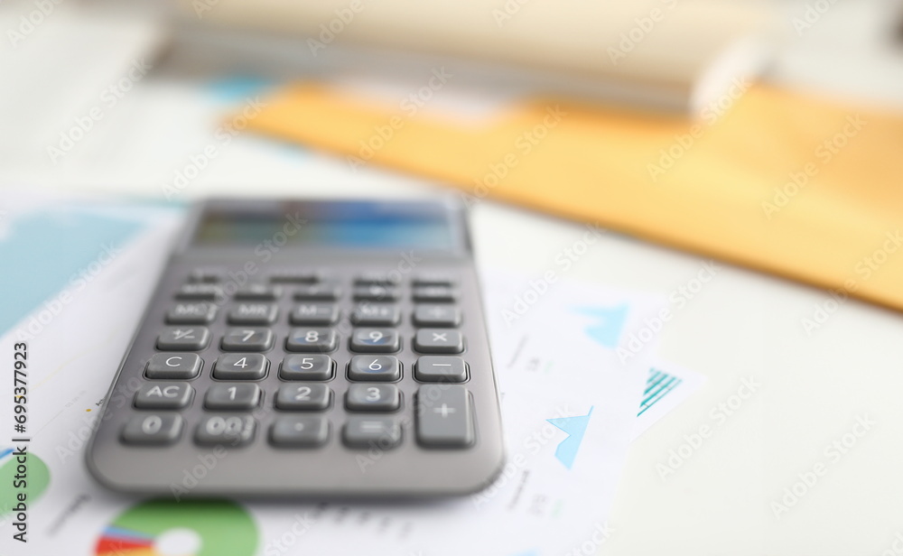 Close-up of black calculator laying on business papers. Equipment to calculate numbers. Tool with buttons on working desktop. Financial report and statistics concept Close-up of black calculator laying on business papers. Equipment to calculate numbers. Tool with buttons on working desktop. Financial report and statistics concept