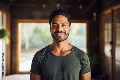 Portrait of a smiling indian man in his 30s dressed in a casual t-shirt against a serene meditation room. AI Generation