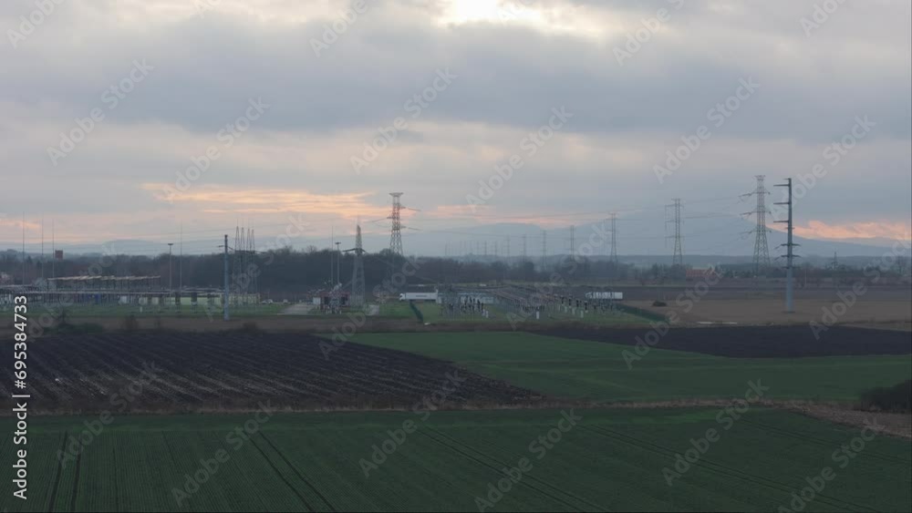 High-angle drone shots and ground-level perspectives unveil a transformer station against a backdrop of sunset clouds. The intricate tapestry of high-voltage poles, lattice structures, cables High-angle drone shots and ground-level perspectives unveil a transformer station against a backdrop of sunset clouds. The intricate tapestry of high-voltage poles, lattice structures, cables