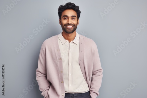 Portrait of a content indian man in his 20s wearing a chic cardigan against a pastel gray background. AI Generation © Markus Schröder