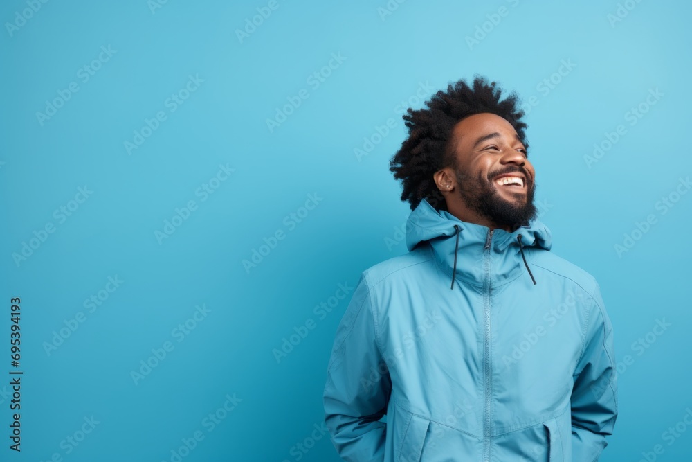 Fototapeta premium Portrait of a cheerful afro-american man in his 30s wearing a functional windbreaker against a soft blue background. AI Generation