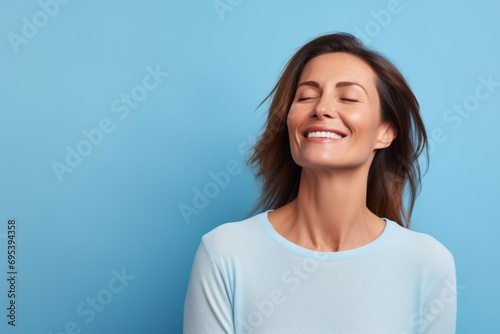 Portrait of a joyful woman in her 40s sporting a long-sleeved thermal undershirt against a soft blue background. AI Generation