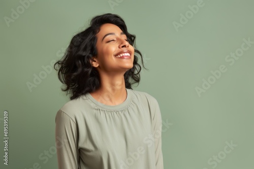 Portrait of a blissful indian woman in her 30s sporting a long-sleeved thermal undershirt against a soft green background. AI Generation