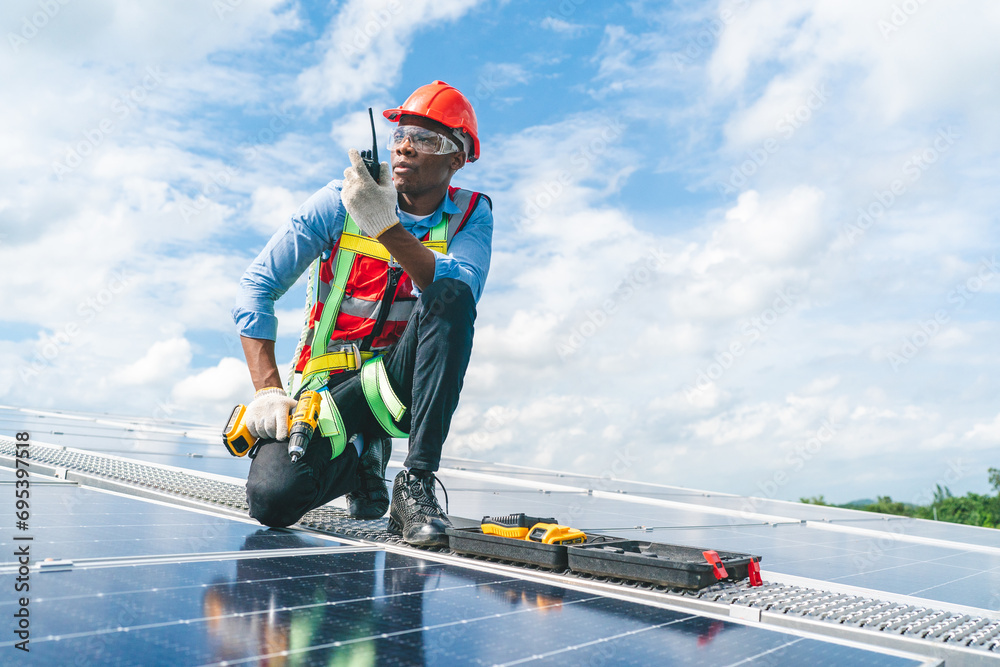 African American engineer maintaining solar cell panels on factory building rooftop. Technician working outdoor on ecological solar farm construction. Renewable clean energy technology concept - obrazy, fototapety, plakaty 