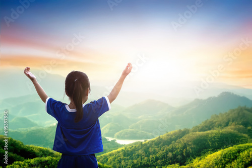 A kid standing on the top of the mountain and raise hands to worship god.