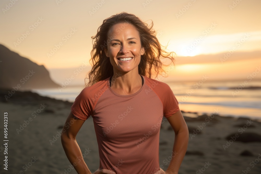 Portrait of a smiling woman in her 30s wearing a moisture-wicking running shirt against a stunning sunset beach background. AI Generation