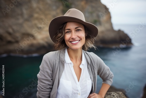 Portrait of a joyful woman in her 40s donning a classic fedora against a spectacular sea cave background. AI Generation