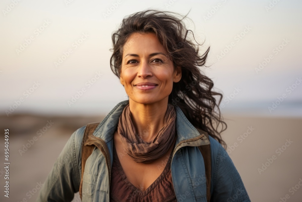 Portrait of a satisfied indian woman in her 50s wearing a rugged jean vest against a serene dune landscape background. AI Generation Portrait of a satisfied indian woman in her 50s wearing a rugged jean vest against a serene dune landscape background. AI Generation