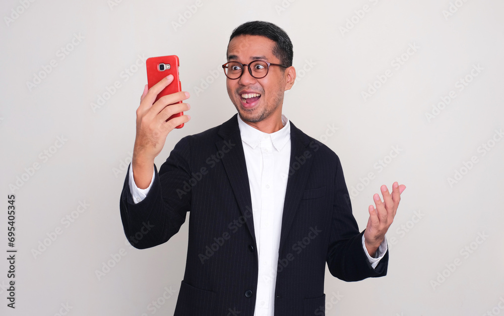 Asian businessman showing amazed expression when looking to phone that he hold Asian businessman showing amazed expression when looking to phone that he hold