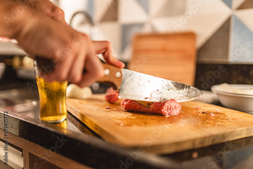 Person cutting sausage on a board. Barbecue. Closeup on hand. photo