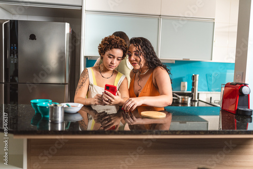 Young women having fun in the kitchen, checking a recipe online.