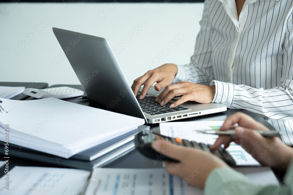 Businesswoman sitting at desk on couch in workplace or at home working on laptop and analyzing data on charts and graphs and writing on papers Businesswoman sitting at desk on couch in workplace or at home working on laptop and analyzing data on charts and graphs and writing on papers