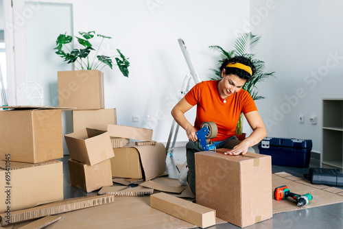 Cheerful woman in red t shirt packing carton box with tape dispenser photo