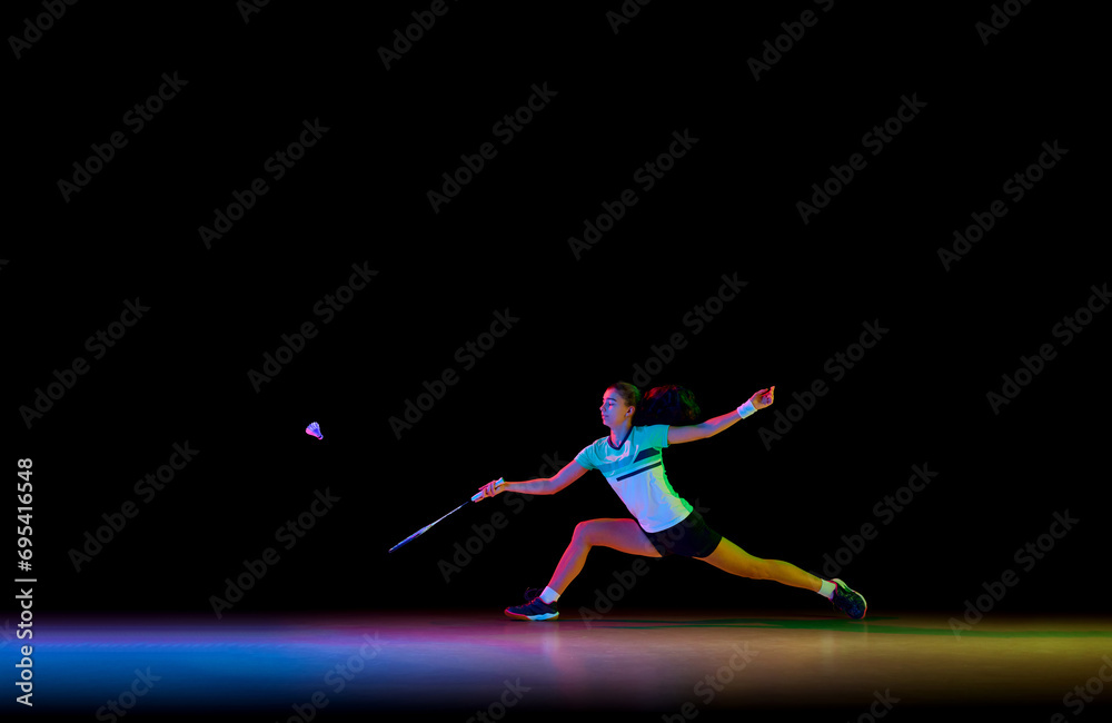 Badminton athlete demonstrates her skills in attack and defense against black background in neon light. Concept of sport, active and healthy lifestyle, strength and power, action. Copy space.