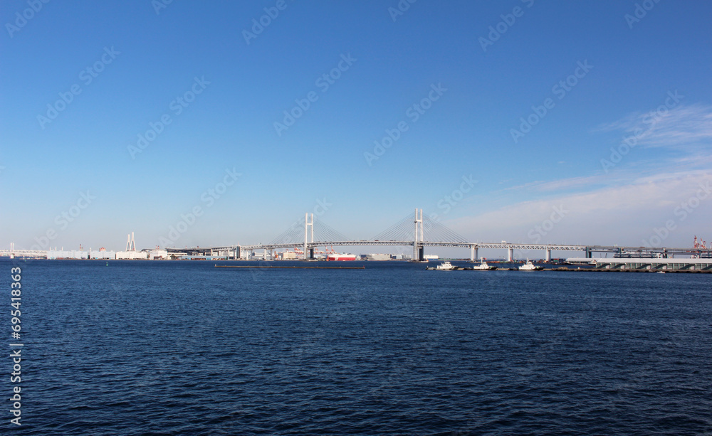 遠くに横浜ベイブリッジが見える風景　雲がほとんど無い青空、青い海にかかる橋
