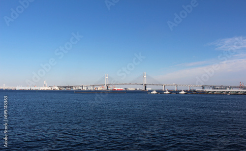 遠くに横浜ベイブリッジが見える風景　雲がほとんど無い青空、青い海にかかる橋 © Eriko Ochiai