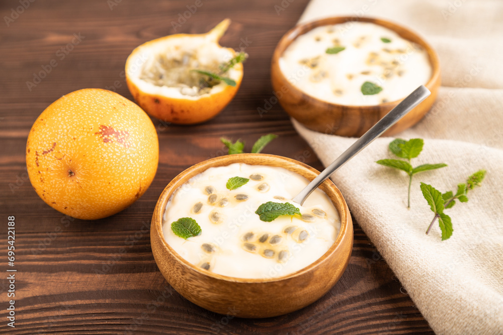 Yoghurt with granadilla and mint in wooden bowl on brown wooden, side view, selective focus. Yoghurt with granadilla and mint in wooden bowl on brown wooden, side view, selective focus.