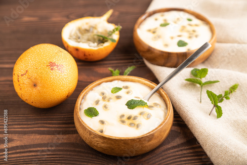Yoghurt with granadilla and mint in wooden bowl on brown wooden, side view, selective focus.