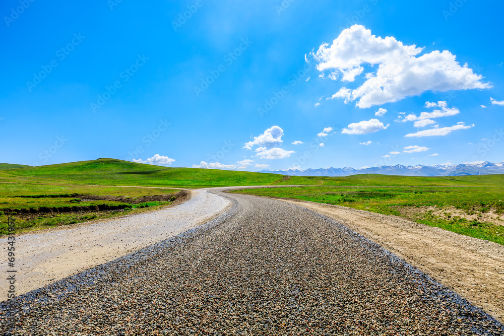Country road and green meadow with mountain nature landscape under blue sky Country road and green meadow with mountain nature landscape under blue sky