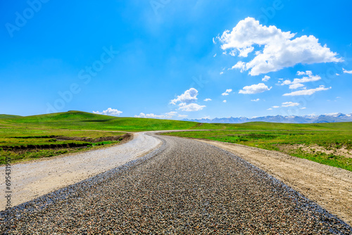 Country road and green meadow with mountain nature landscape under blue sky