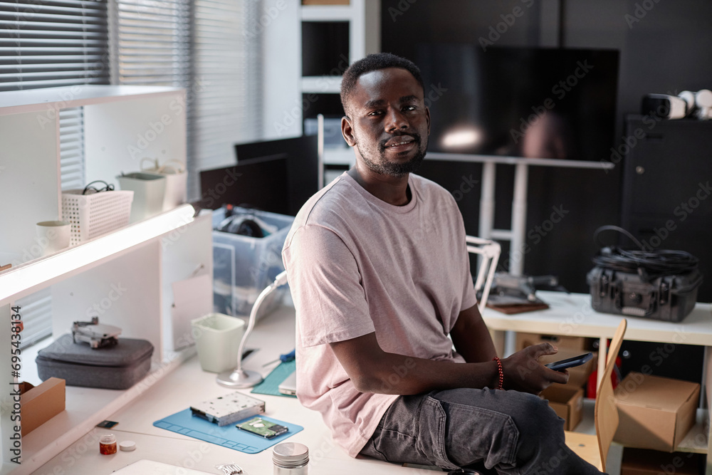 Portrait of Black adult man smiling at camera at workplace in tech repair shop, copy space Portrait of Black adult man smiling at camera at workplace in tech repair shop, copy space
