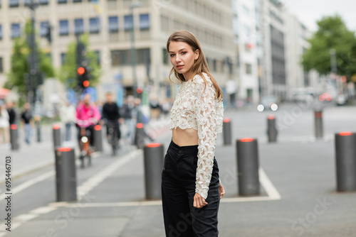 young woman posing in lace top and high waist pants standing on street in Berlin in daylight