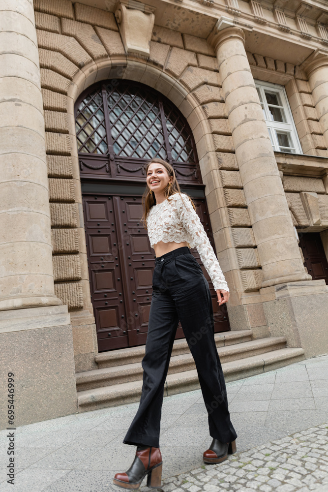 pleased young woman in lace top and high waist pants looking at camera on urban street in Berlin