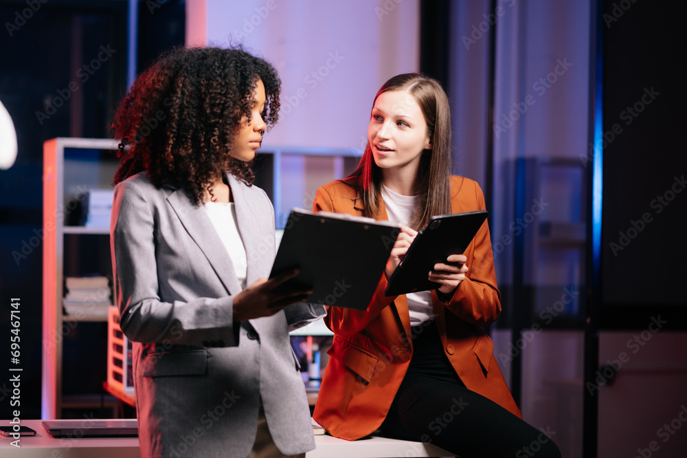 Kind leader executive manager share and discuss business solutions plan ideas on tablet with African female marketing manager. neon light in dark time.