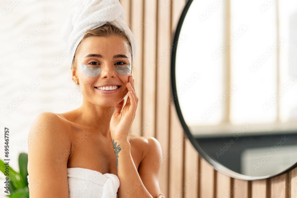 Happy woman with eye patches after shower, wearing white towel, standing in bathroom near mirror Happy woman with eye patches after shower, wearing white towel, standing in bathroom near mirror