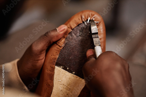 Above angle of hands of young black man fixing leather with nails and pliers on sole of boot or shoe while working over new footwear photo
