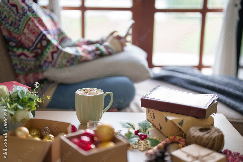 Young asian woman surfing social media on smartphone and cup of hot chocolate with marshmallow on table while sitting on couch in living room decorating xmas ornaments for celebrate christmas festive Young asian woman surfing social media on smartphone and cup of hot chocolate with marshmallow on table while sitting on couch in living room decorating xmas ornaments for celebrate christmas festive