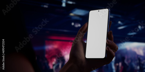 Caucasian woman holding phone, night club in the background, blank screen mockup
