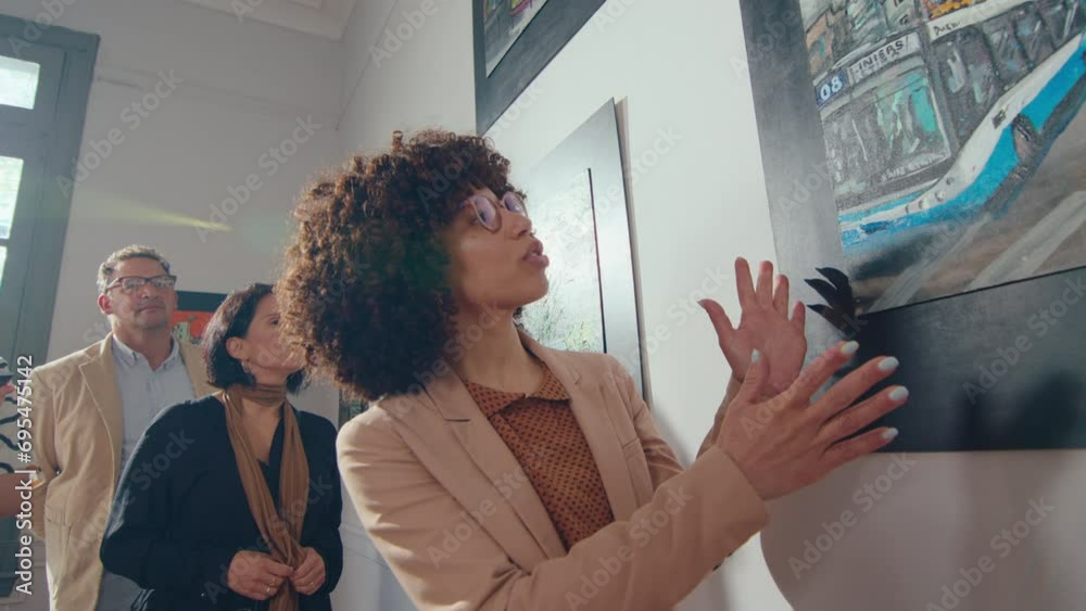 female-tour-guide-pointing-at-painting-hanging-on-the-wall-in