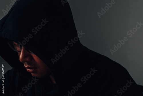 A male hacker wearing glasses and a hoodie covers his head in the dark is hacking into a victim's financial system. Data thief, internet fraud, darknet and cyber security concept. photo